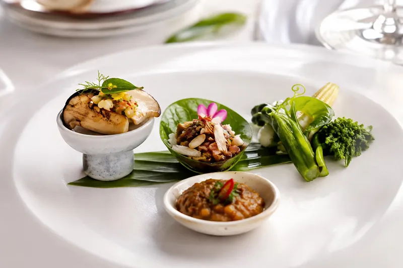 Three signature bites on a white plate: king oyster mushroom with green mango relish, miang kham, and Thai vegetables with a chili dip