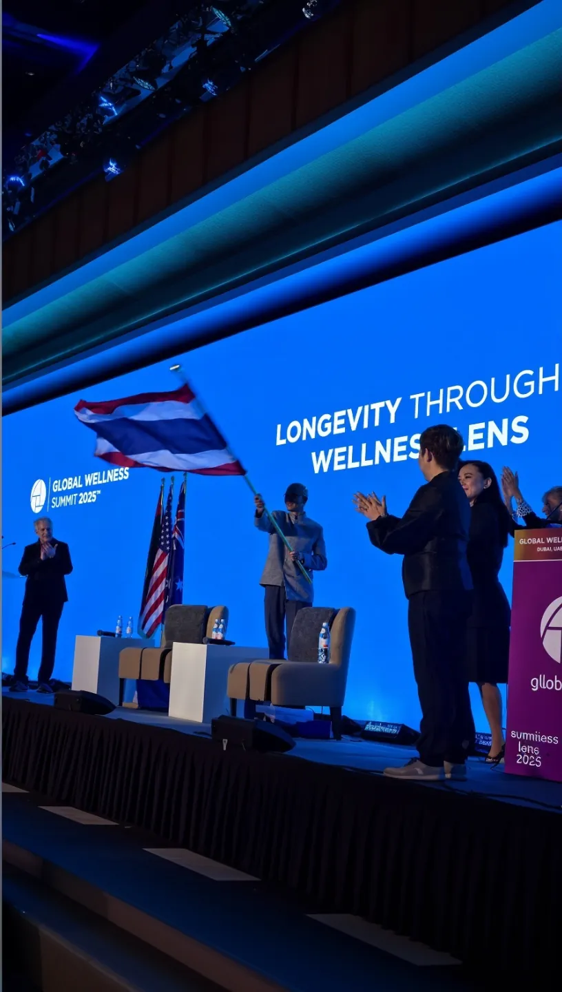 Speakers applauding beside the Thai flag on the Global Wellness Summit 2025 stage, under a screen reading "Longevity Through Wellness Lens"